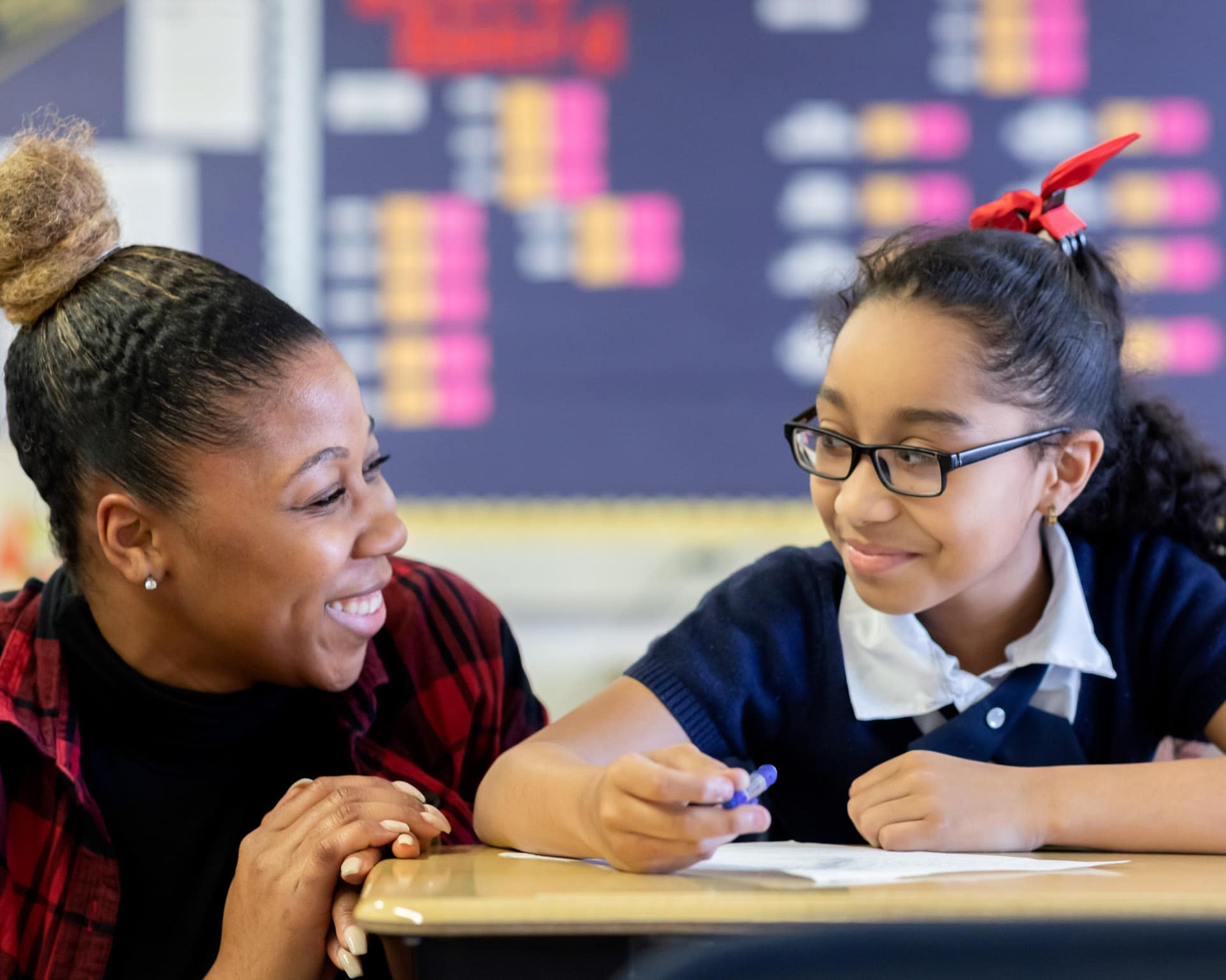 Teacher speaking with a young scholar at a classroom desk