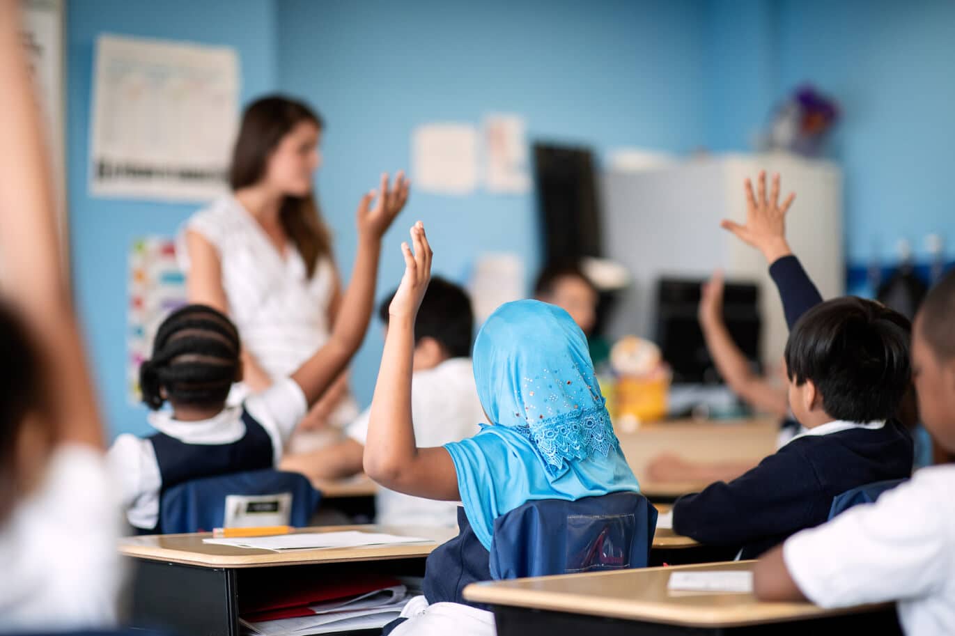 Teacher leading a class with scholars raising their hands
