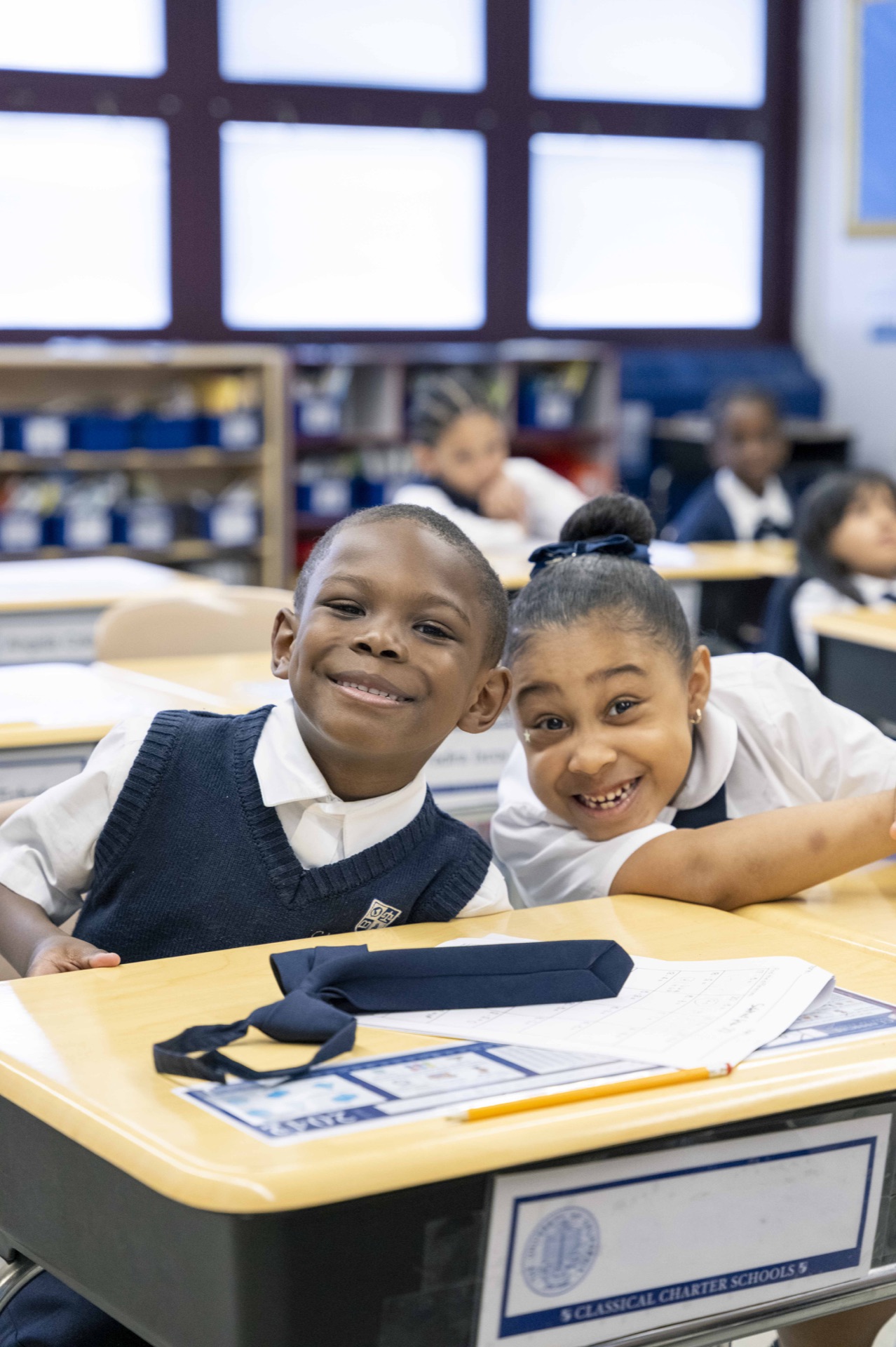 Two Classical scholars smile together at their classroom desk.