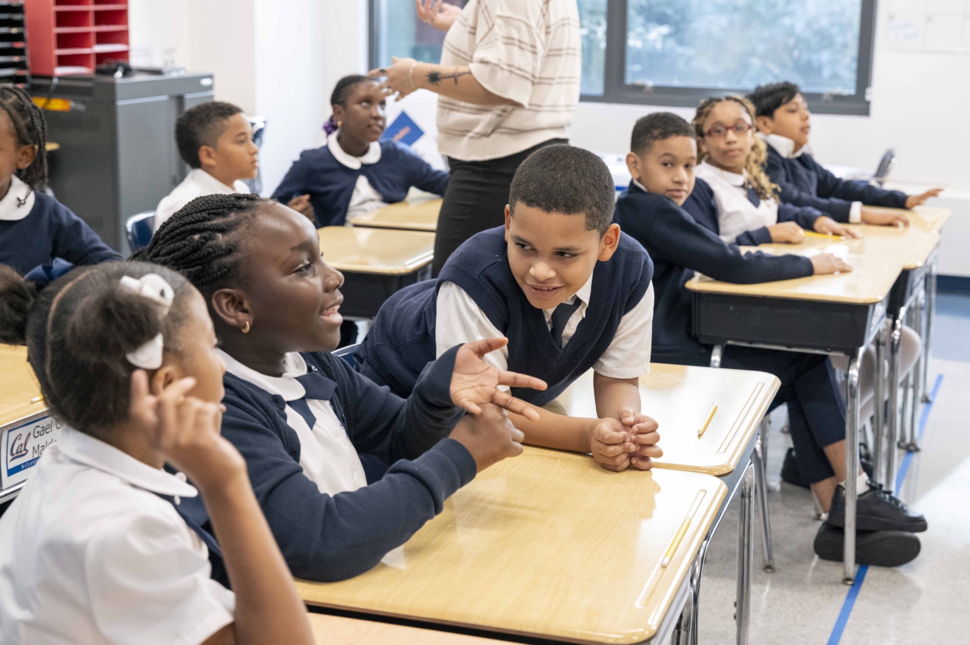 Classical scholars discuss their work together at classroom desks.